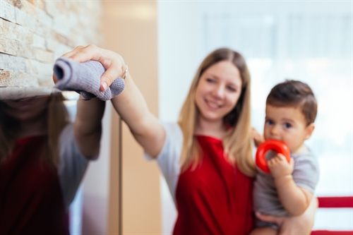 Woman holding a toddler as she cleans a TV screen with a microfibre cloth.