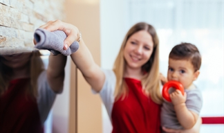 Woman holding a toddler as she cleans a TV screen with a microfibre cloth.