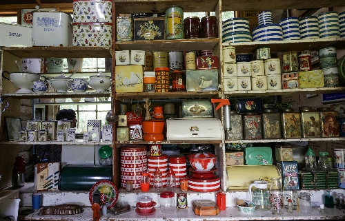 a collection of tins and vintage storage kept on cluttered shelves with a window behind.