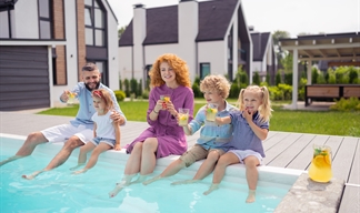 A family sitting on the side of a garden swimming pool dangling their legs in the water